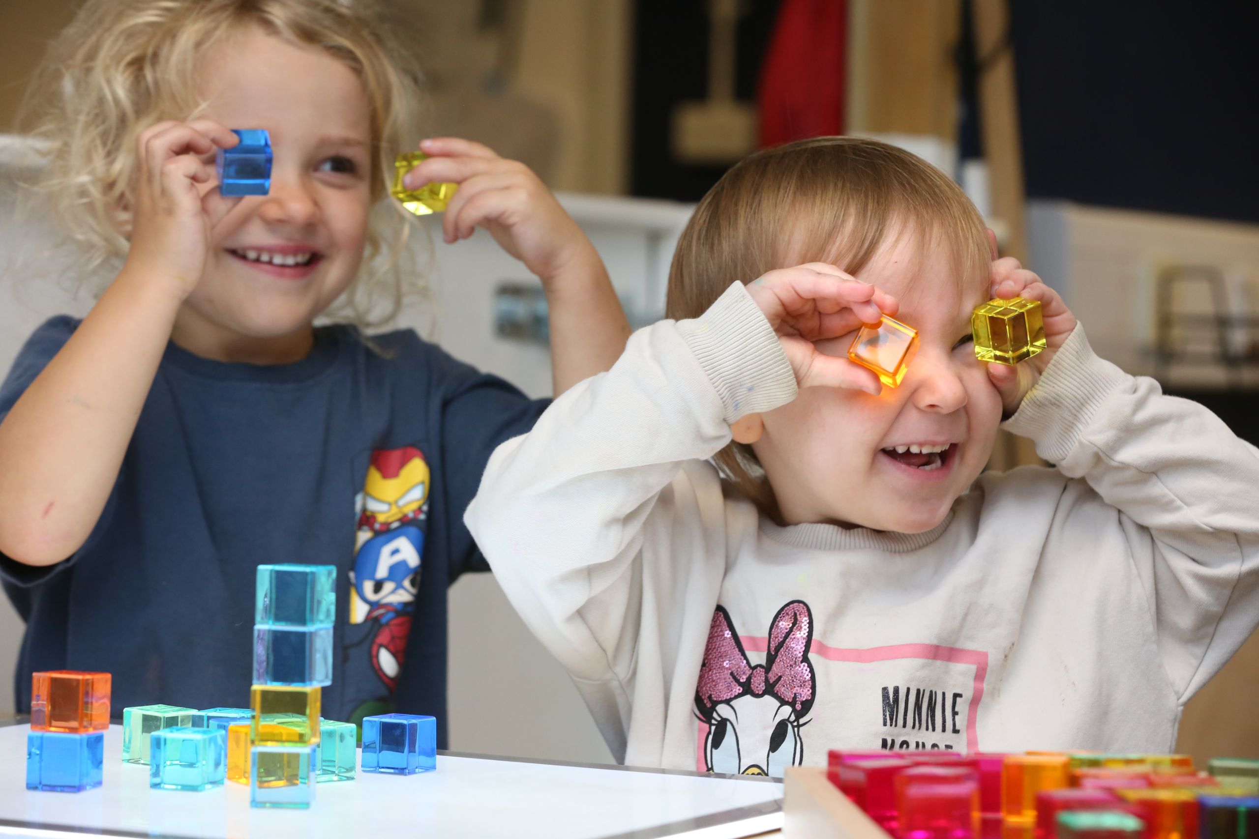 Smiling children enjoying playful learning with colourful translucent blocks, stacking and holding them to their faces.